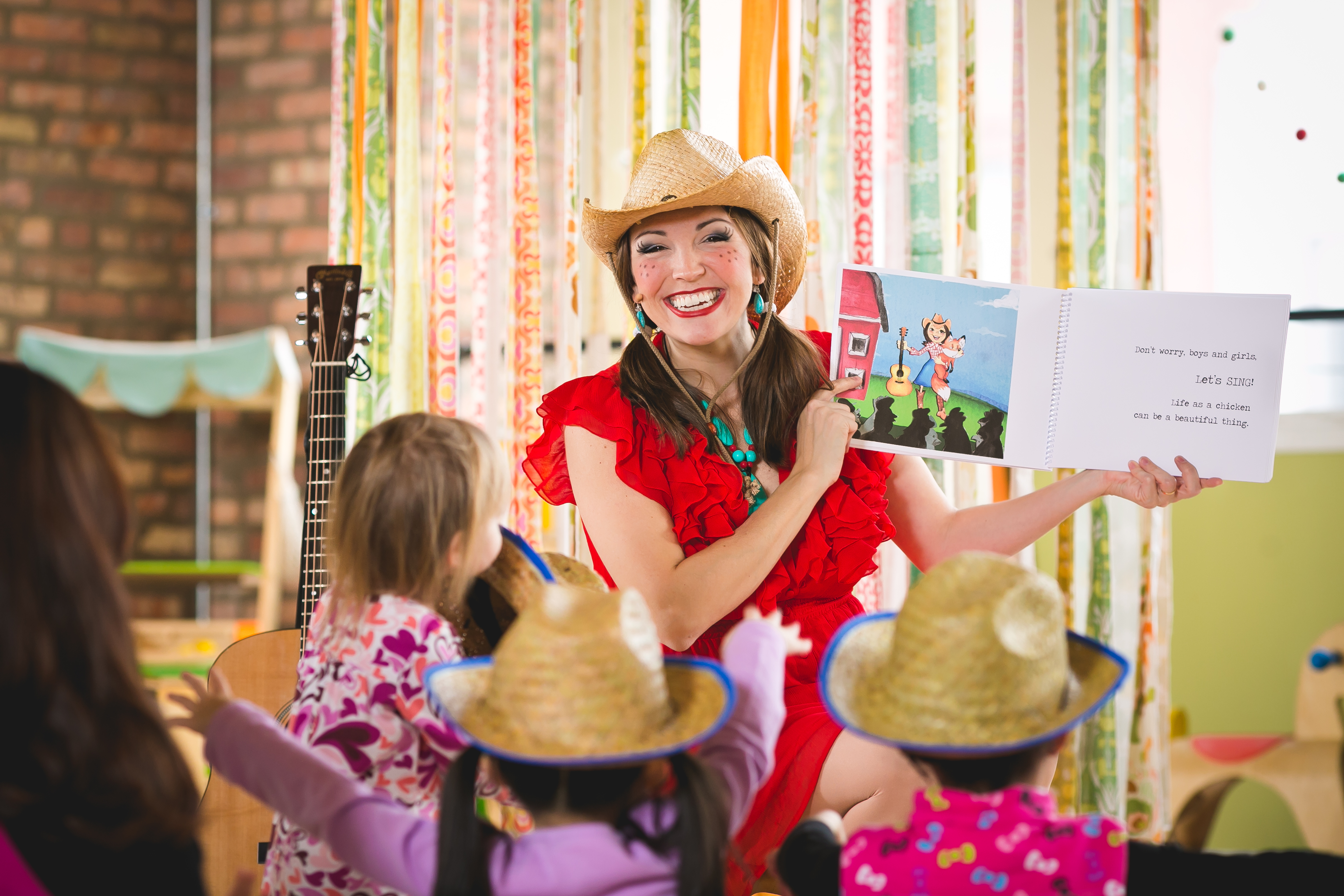 Miss Jamie holding up an oversized picture book for children in straw hats